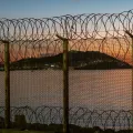 Ceuta, cidade espanhola no norte da África, vista do Marrocos atrás de uma cerca de arame espinhoso localizada na fronteira marroquina, contra um deslumbrante pôr do sol sobre o mar. Crédito: Shutterstock