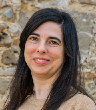 Retrato da professora e investigadora Ioli Campos, sobre uma parede de pedra.