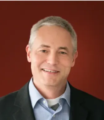 Retrato de Keith Johnson, autor da revists internacional Foreign Policy, sobre um fundo vermelho escuro.