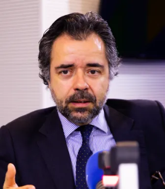 Imagem de um homem sentado, num estúdio de rádio, com um microfone à frente.