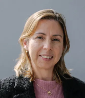 Uma mulher loira, sorridente, com um colar ao pescoço. D/R.