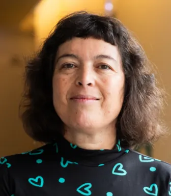 Retrato da psiquiatra Manuela Silva a sorrir. Fundo amarelo.