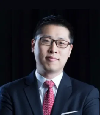 Um homem de fato, com uma gravata vermelha, e de óculos, sob um fundo preto.