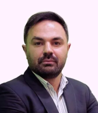 Imagem a cores de um homem, o investigador Arash Reisinezhad, vestido com um fato. Fundo rosa claro.