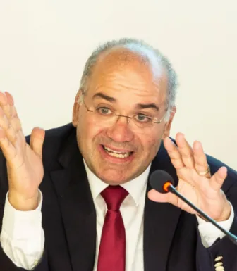 Retrato de um homem, o historiador José Eduardo Franco, a falar para um microfone e a gesticular.