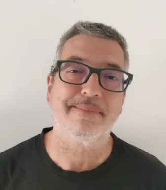 Retrato de um homem de óculos e camisola preta. Fundo claro.