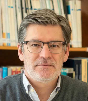 Imagem a cores de um homem, Paulo Miguel Rodrigues, com uma estante de livros a servir de fundo.