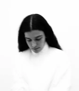 Imagem a preto e branco da artista Silly, a olhar para baixo e vestida de branco.