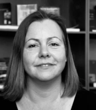 Retrato a preto e branco da socióloga Tatiana Moura. Uma estante com livros e fotografias a cobrir o fundo.