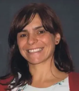 Imagem de uma mulher sorridente, vestida com uma camisola com um padrão e um casaco vermelho.