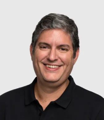 Retrato de um homem, a sorrir, vestido com uma camisola preta. Fundo cinzento claro.