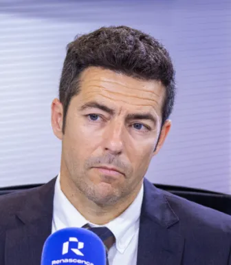 Imagem de um homem sentado, a falar para um microfone, num estúdio de rádio.