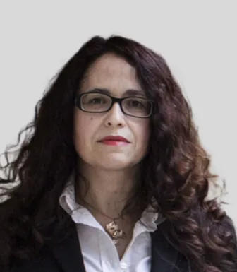 Imagem de uma mulher, vestida com uma camisa branca e um casaco preto, com um colar ao pescoço.