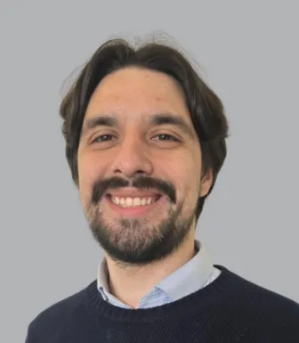 Imagem de um rapaz sorridente, vestido com um polo e uma camisa. Fundo conzento.