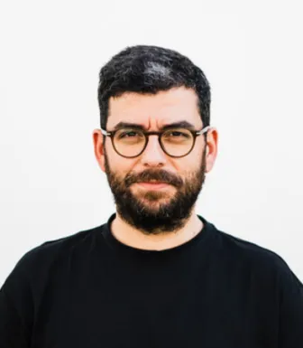 Imagem de um homem, com barba, e de óculos. Vestido com uma t-shirt preta.
