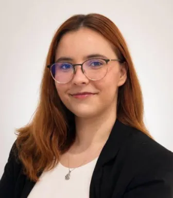 Retrato a cores de uma rapariga, de óculos e cabelo castanho claro, vestida com uma camisola branca e um blazer preto.