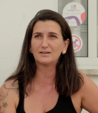 Retrato de uma mulher, vestida com um top preto e uns brincos dourados.