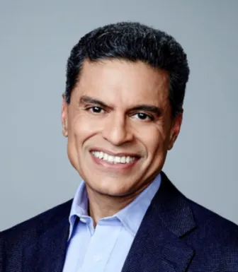 Imagem de um homem a sorrir, vestido com uma camisa azul claro e um casaco azul escuro. Fundo cinzento.
