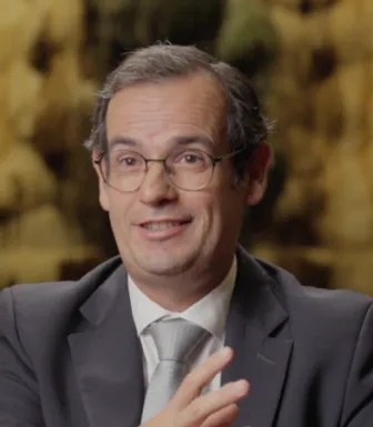 Retrato de homem que usa óculos, vestido com um fato e uma gravata cinzenta.