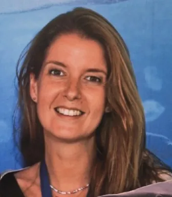 Retrato a cores de uma mulher, sorridente, de cabelo castanho claro, sobre um fundo azul.