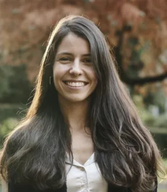 Retrato a cores de uma mulher sorridente. Tem cablo comprido e uma camisa branca.
