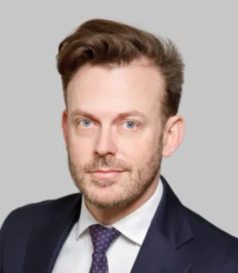 Retrato a cores de um homem de olhos azuis e cabelo castanho. Veste um fato azul. Fundo cinzento claro. Créditos:CNAS