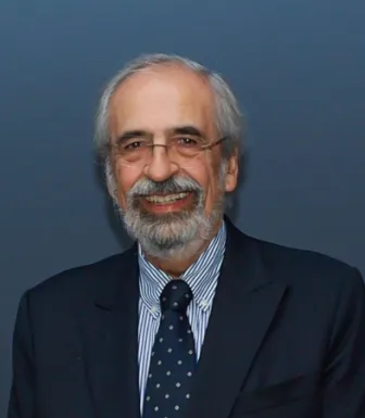Retrato a cores de um homem de cabelo e barba grisalho, vestido de fato. Fundo azul.