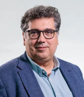 Retrato a cores de um homem, de óculos, com expressão sorridente. Veste uma camisa azul. Créditos: Reinaldo Rodrigues
