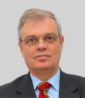 Retrato a cores de um homem de óculos e cabelo grisalho, vestido com um fato preto, uma camisa azul e uma gravata vermelha e verde. D/R