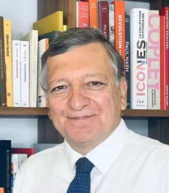 Retrato a cores de um homem, Durão Barroso, a sorrir, vestido com uma camisa branca. Uma estante de livros cobre o fundo. Créditos: EUI