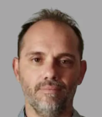 Retrato a cores de um homem de cabelo escuro e barba grisalha. Fundo cinzento. D/R