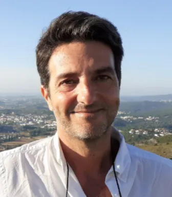 Retrato a cores de um homem a sorrir sobre uma paisagem. 