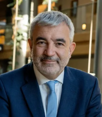 Retrato a cores de um homem a sorrir, com cabelo e barba grisalhos. Veste um fato azul escuro e uma gravata azul clara. 