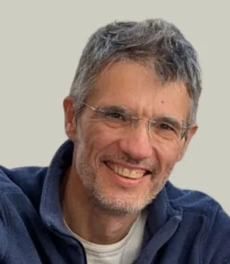 Retrato a cores de um homem que usa óculos e tem o cabelo grisalho. Veste uma camisola azul.