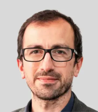 Retrato a cores de um homem com óculos e cabelo escuro. Fundo cinzento claro.