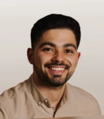 Retrato a cores de um rapaz jovem, com cabelo e barba escura, sobre um fundo bege. D/R
