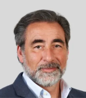 Retrato a cores de um homem, a sorrir, com barba e cabelo grisalhos. Fundo cinzento claro. D/R
