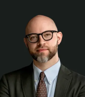 Retrato a cores de um homem sobre um fundo preto. Tem barba, usa óculos e um fato. Créditos: Foreign Policy