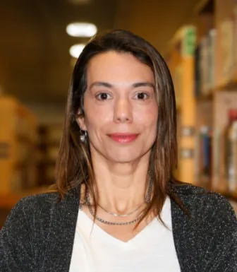 Retrato a cores de uma mulher, num corredor de uma biblioteca. Tem cabelo castanho e está a sorrir.  D/R