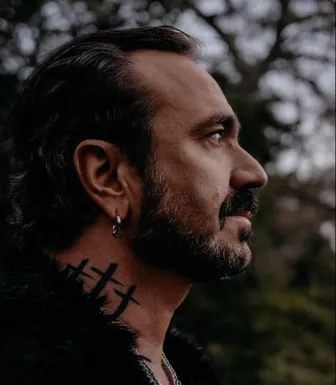 Imagem de perfil de um homem de barba, com tatutagens no pescoço, o músico Fernando Ribeiro, fundador dos Moonspell