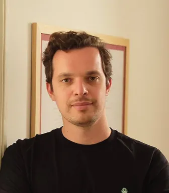 Imagem de um homem, o maestro Martim Sousa Tavares, vestido com uma t-shirt preta sob um fundo bege.