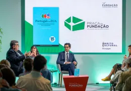 Imagem de quatro pessoas a conversar perante uma plateia,  sob um fundo verde.