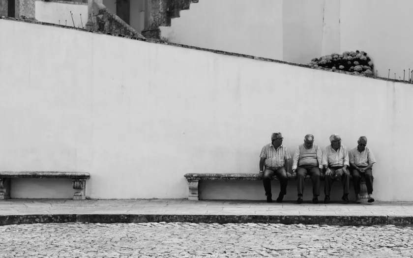 Imagem de idosos sentados, junto a um banco vazio