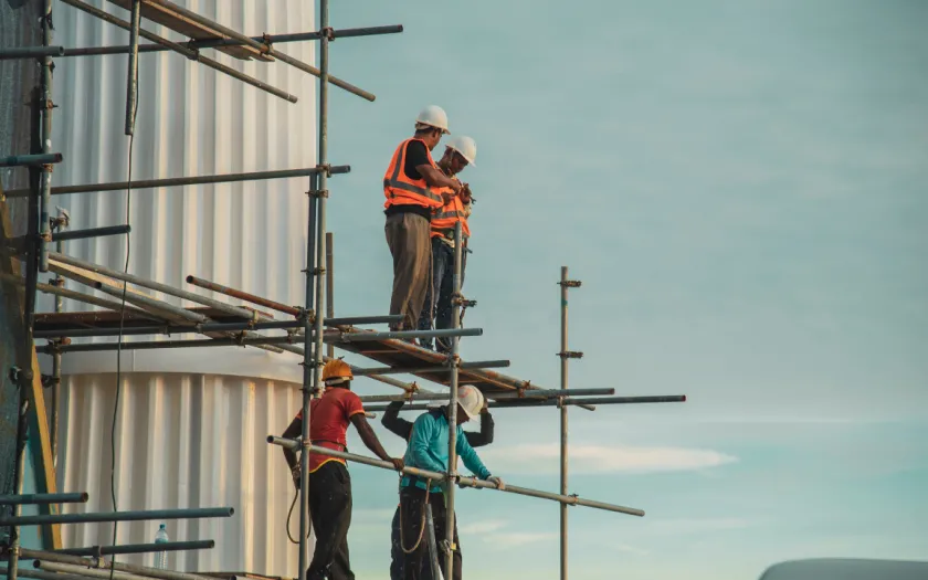 Imagem de trabalhadores da construção civil num andaime de um prédio em construção.