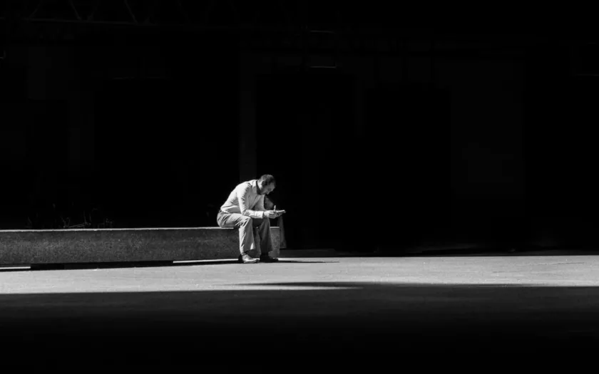 Imagem de um homem triste sentado num banco sozinho. D/R