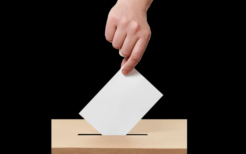 Imagem de uma mão a colocar o voto na urna eleitoral. Crédito: Canva