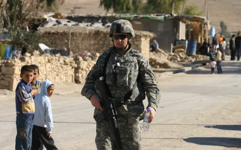 em grande plano um soldado norte-americano junto a uma estrada no Iraque, enquanto ao fundo várias crianças apontam para o militar. Crédito: Shutterstock