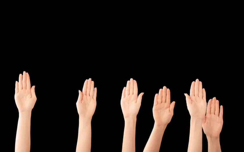 várias mãos no ar, sob um fundo preto, mostrando participação eleitoral. Crédito: Canva