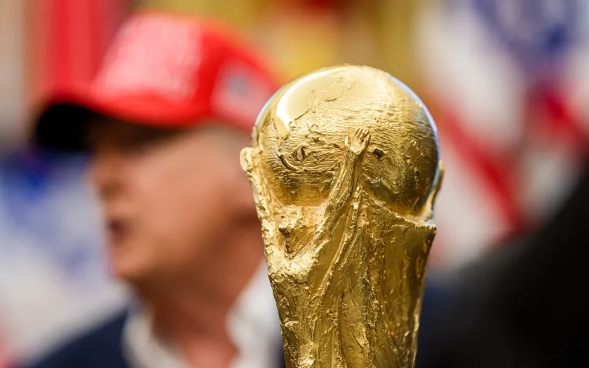 Imagem do troféu do Mundial 2026 em foco e, ao fundo, desfocado, Donald Trump. Créditos: shutterstock