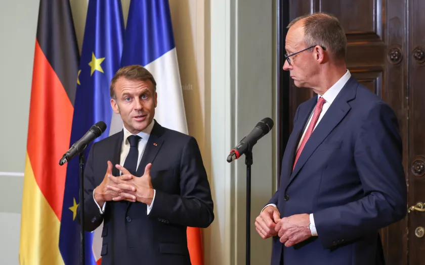 Emmanuel Macron e Friedrich Merz, lado a lado, durante uma conferência de imprensa conjunta. Bandeira de França, Alemanha e da UE ao Fundo. Créditos: shutterstock